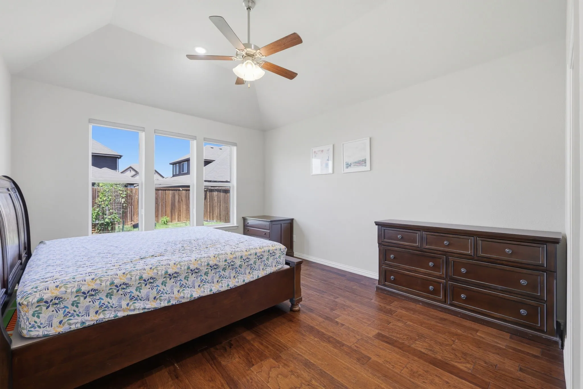 Bedroom featuring vaulted ceilings, wood-finish flooring, a ceiling fan, and a three-pane window with backyard outlook