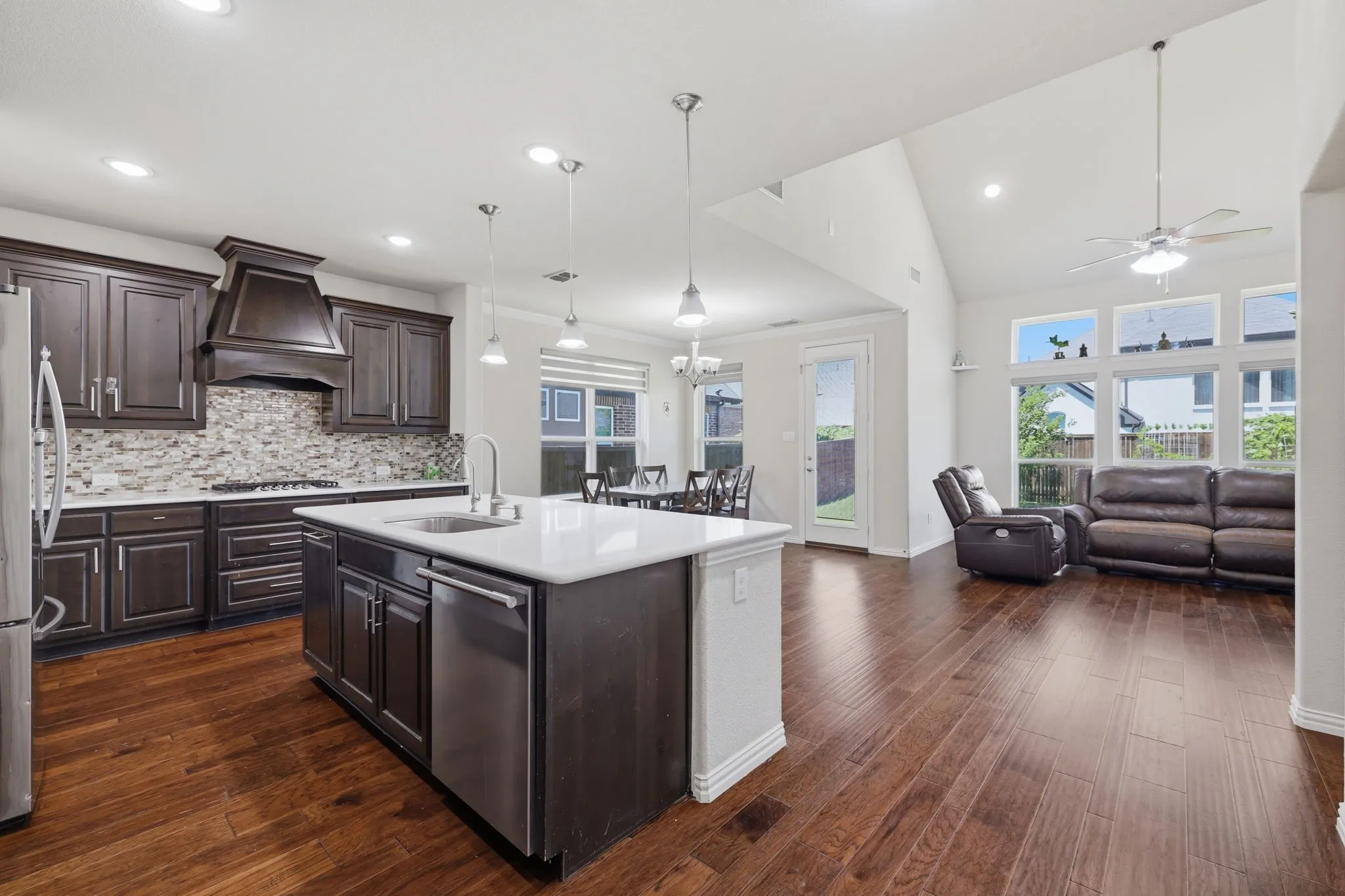Modern kitchen featuring dark wood cabinetry, a tiled backsplash, stainless steel appliances, and a central island with a sink and white countertop