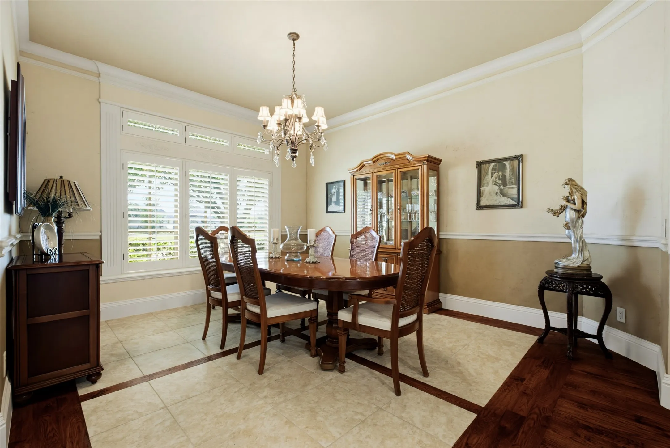 Crown molding, two-tone wall treatment, wood-finish flooring with tile inlay, chandelier light fixture, and plantation shutters