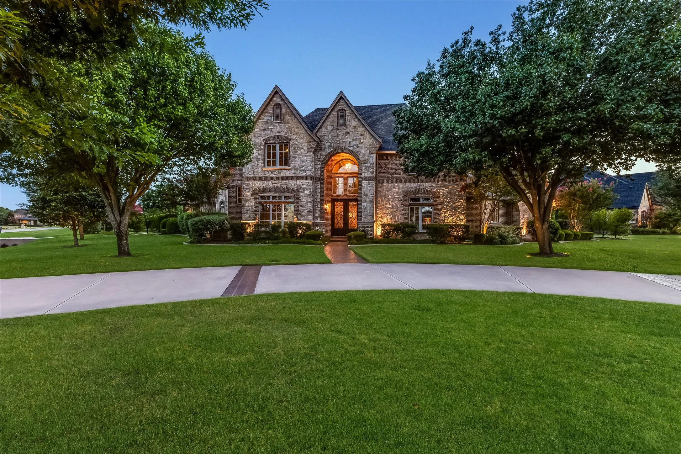 Stone exterior with multiple gables, arched entry, and integrated landscape lighting