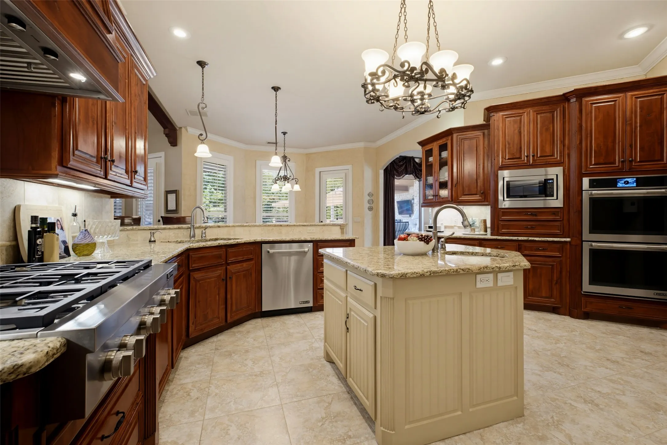 Gourmet kitchen featuring wood cabinetry, stone countertops, stainless steel appliances, a center island with a sink, and tile flooring