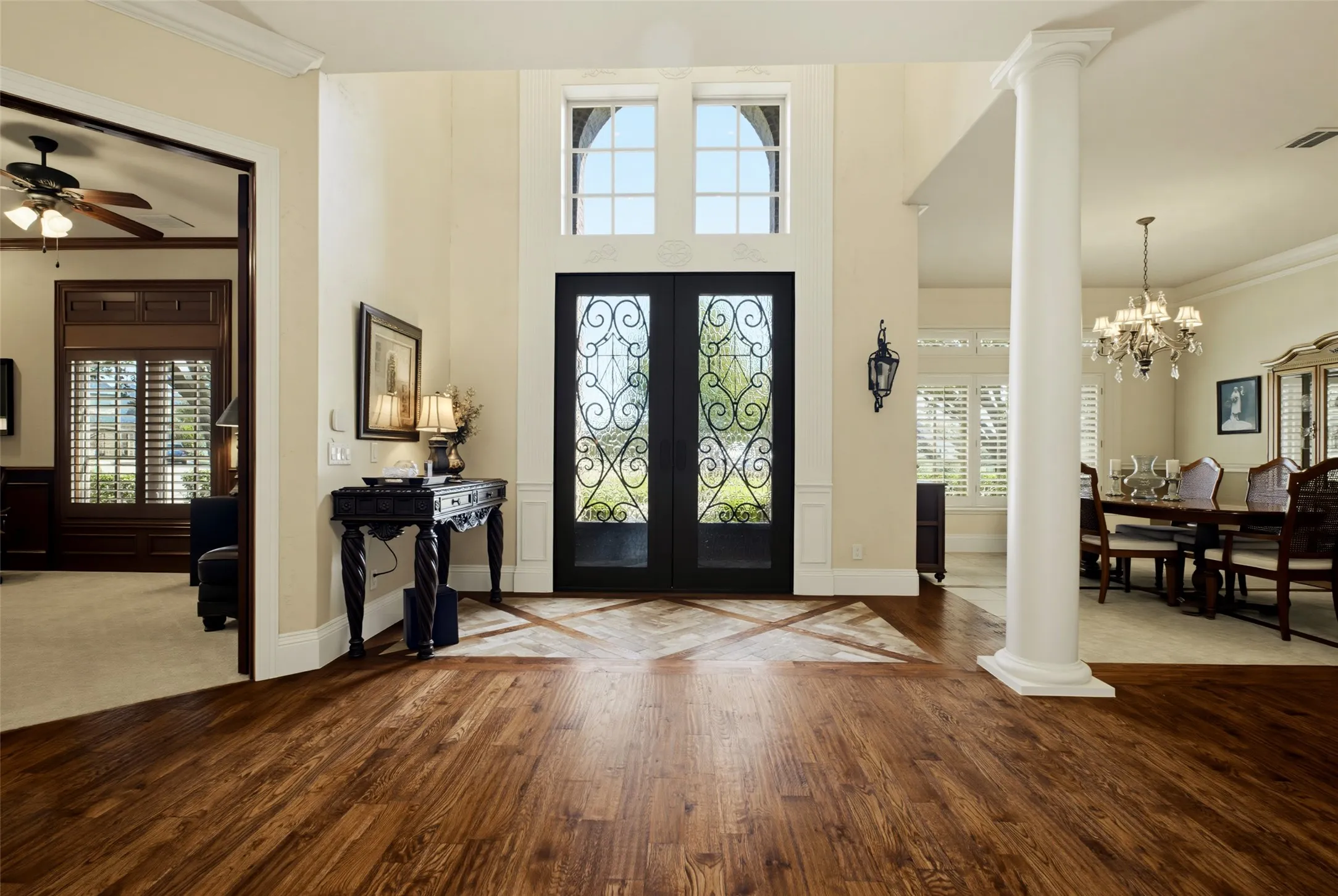 Grand entry featuring a two-story ceiling, decorative iron-insert double doors, and rich wood-finish flooring with a contrasting inlay
