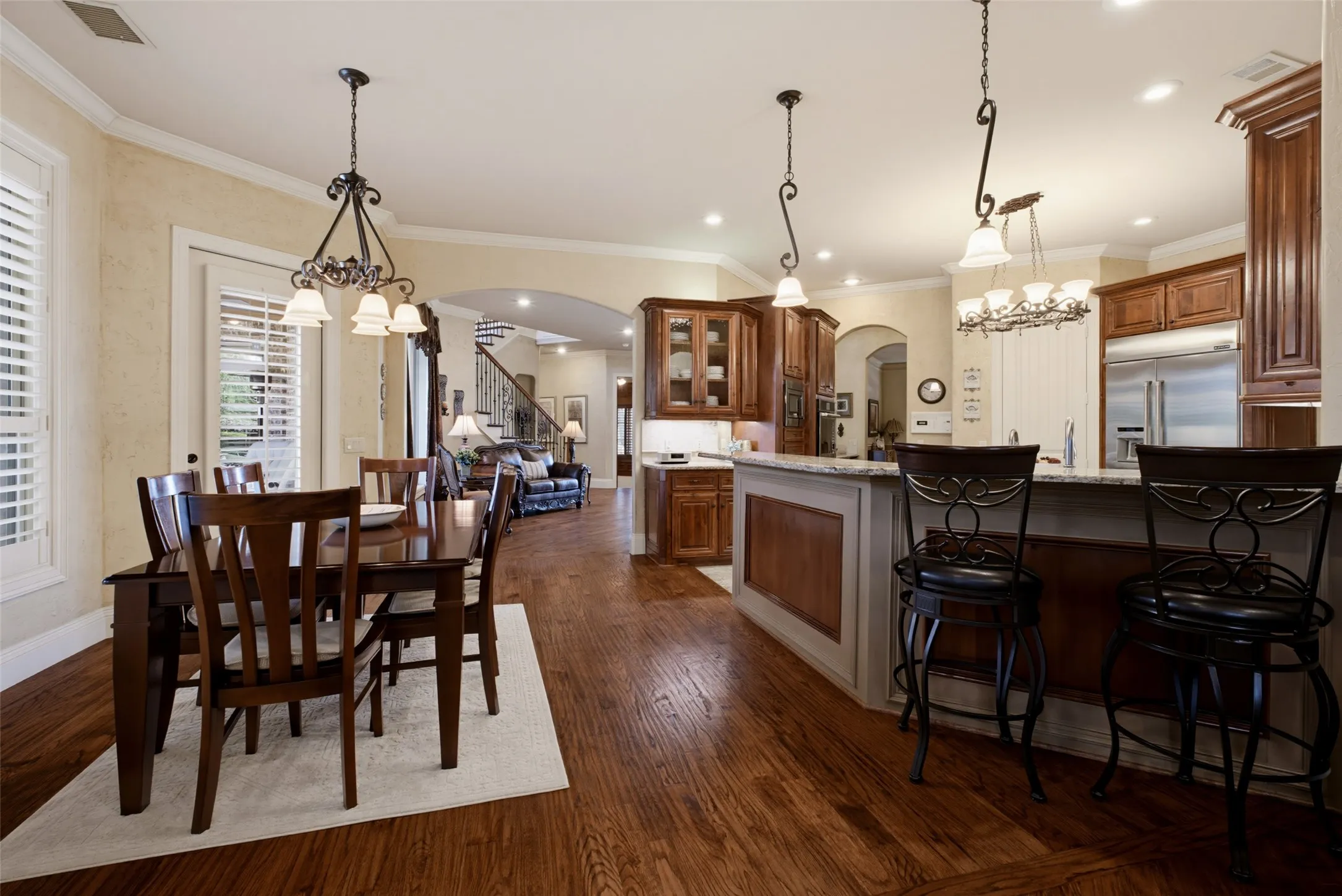 Hardwood flooring extending throughout, kitchen island with seating, pendant lighting, recessed lighting, and crown molding