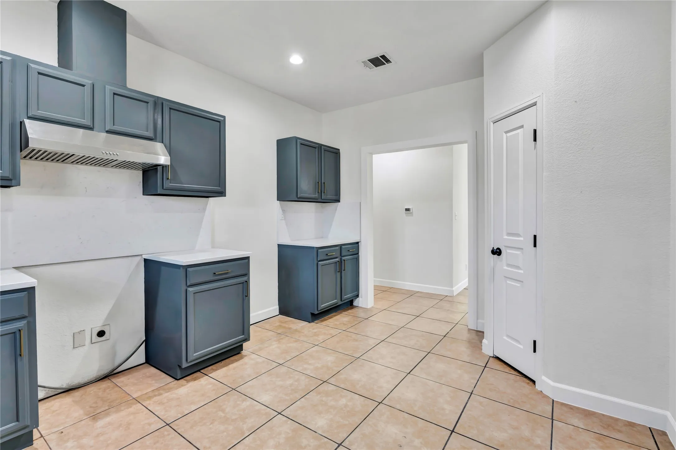 Kitchen featuring blue-grey cabinetry with white countertops, a stainless steel range hood, and tile flooring