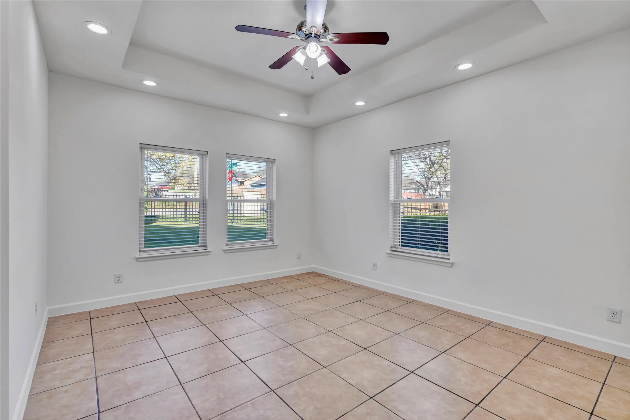 Spacious room featuring tile flooring, white walls, and a recessed tray ceiling with integrated lighting