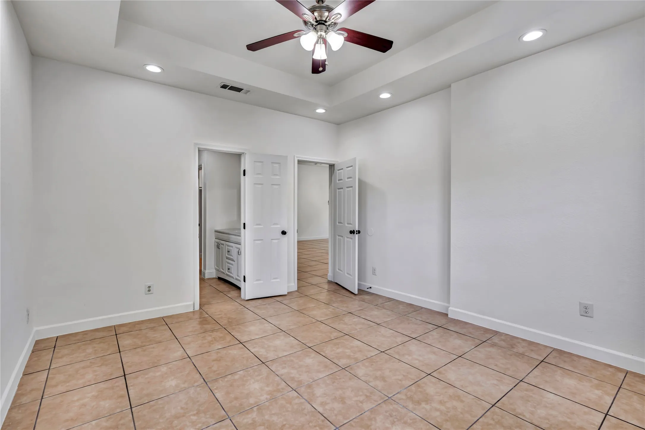 Spacious room featuring tile flooring, a tray ceiling, recessed lighting, and a ceiling fan with integrated light fixture