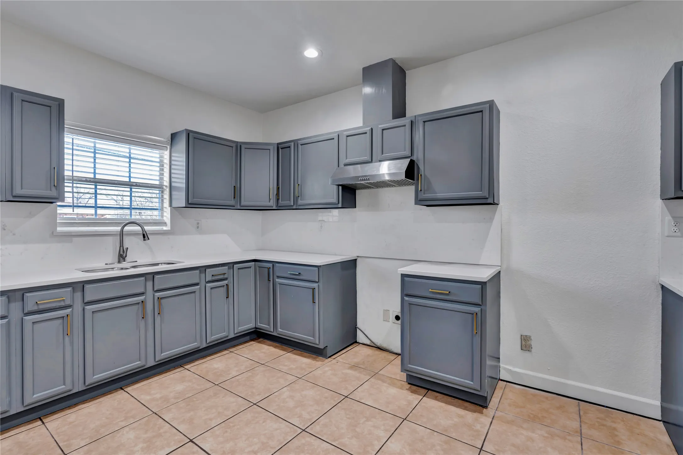 Kitchen featuring gray cabinetry, white countertops, tile flooring, a stainless steel range hood, and a window with blinds