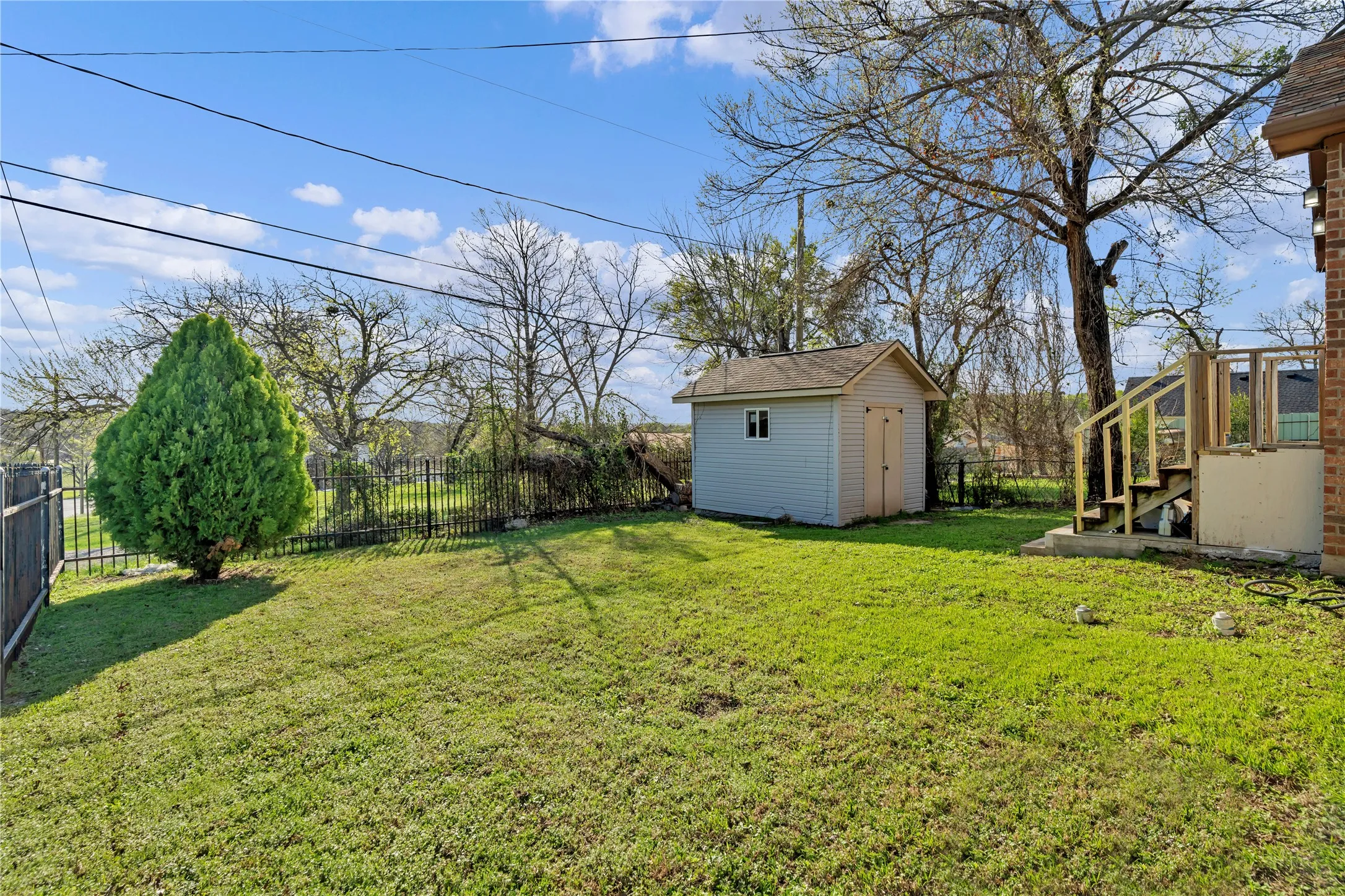 Expansive rear yard featuring green lawn, a light blue storage shed with white trim, a black metal fence, a privacy fence, and a multi-level wooden deck structure