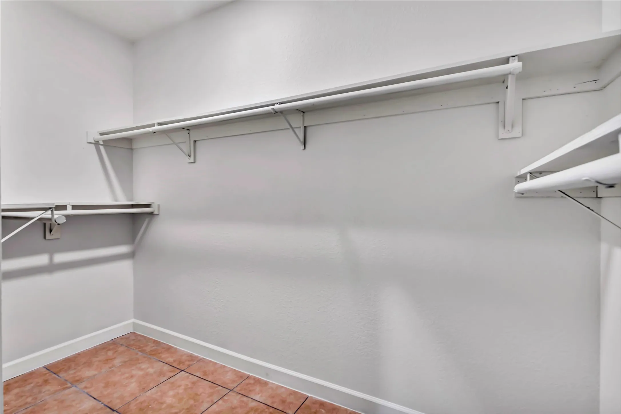Interior closet featuring tile flooring, white baseboards, white walls, and multiple white-painted wooden shelving units with hanging rods