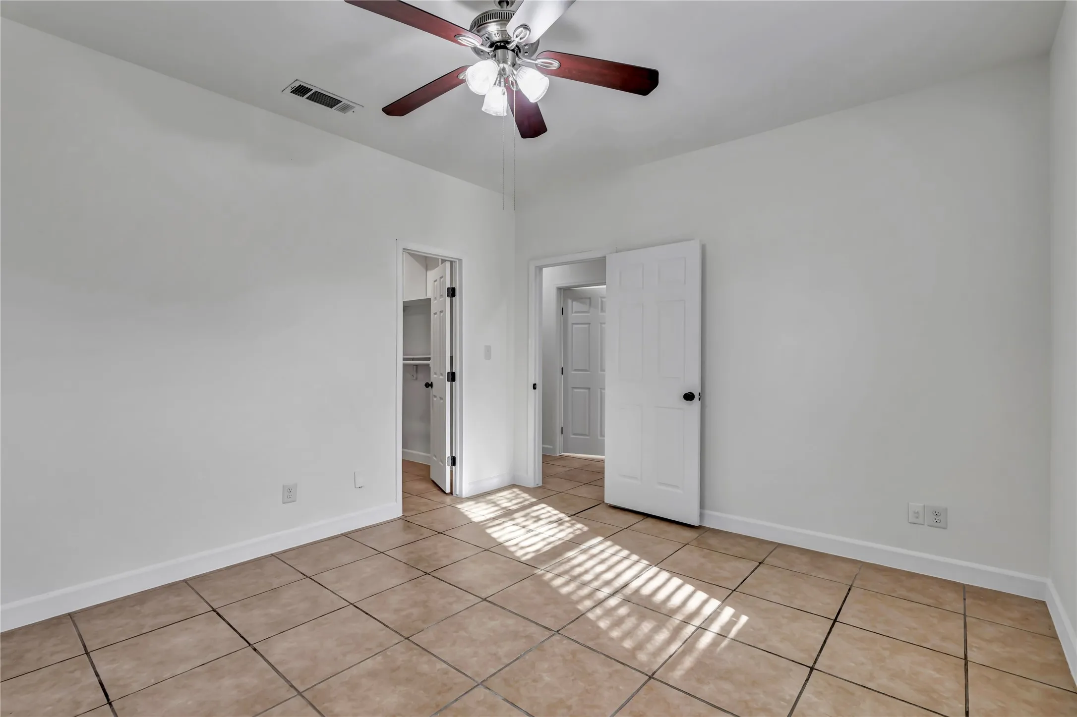 Spacious room featuring neutral-toned tile flooring, white walls, and a ceiling fan with integrated lighting