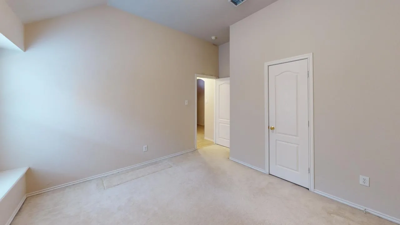 Interior room featuring a vaulted ceiling, neutral-toned walls, and plush carpet flooring