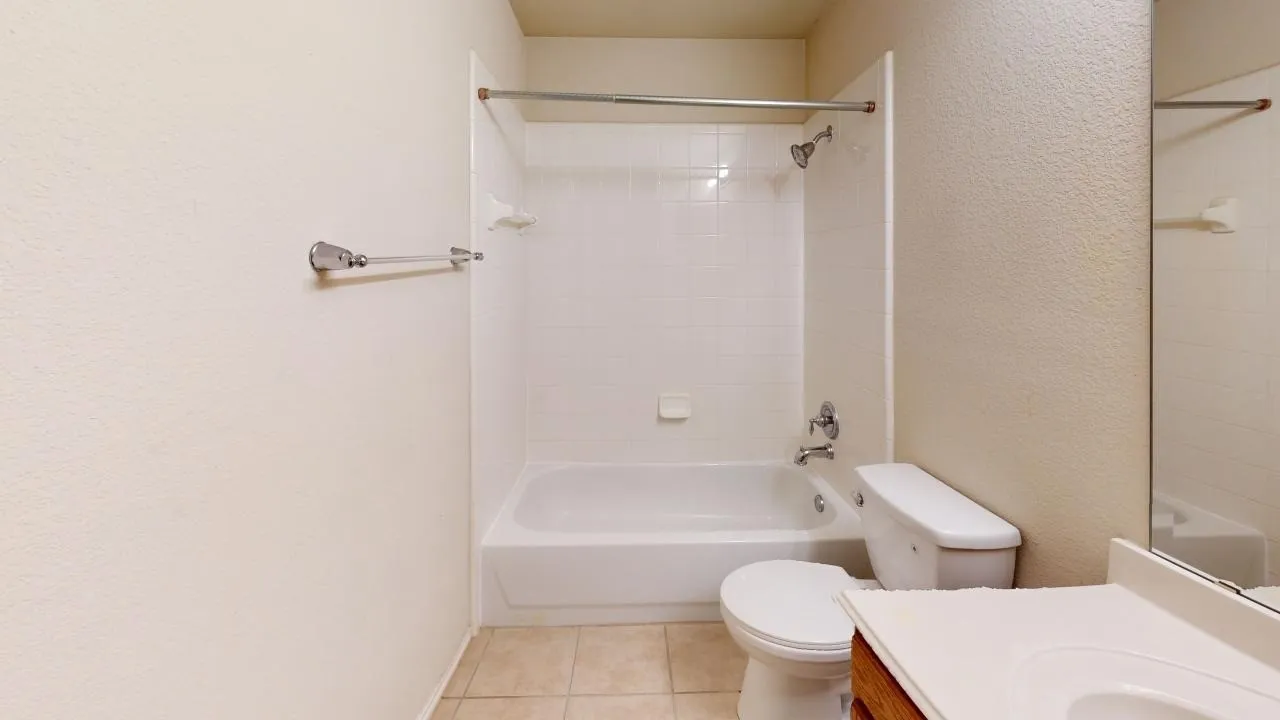 Bathroom featuring a white bathtub, ceramic tile shower surround, toilet, and vanity with an integrated sink