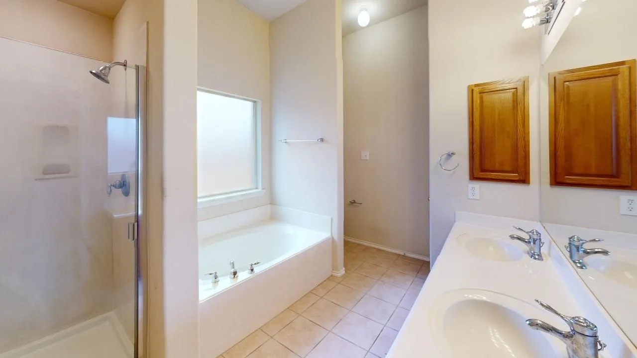 Bathroom featuring a dual vanity with integrated sinks, a built-in soaking tub, a separate shower with glass enclosure, and wood-finish cabinetry