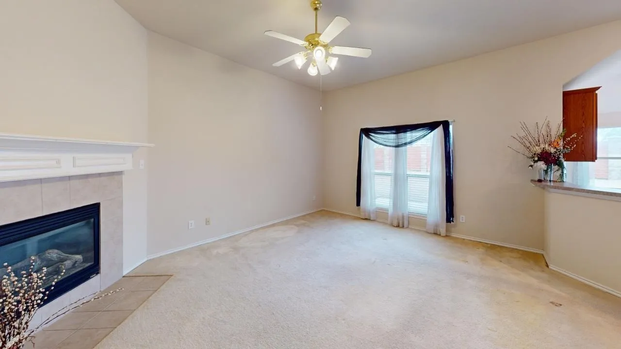 Spacious living area featuring a fireplace with a light-colored tile surround and mantle, vaulted ceiling, ceiling fan with integrated lighting, and carpet flooring
