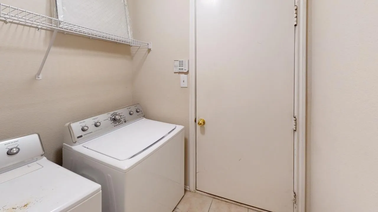 Utility area featuring tile flooring, neutral wall tones, a solid door with brass hardware, and a wall-mounted shelving unit