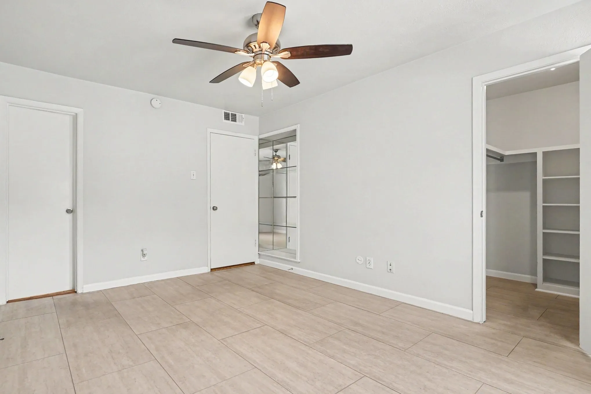 This primary bedroom view shows the walk-in closet to the right, the main entrance door at the center, and the bathroom door to the left.  Behind the main door with a mirrored built-in shelf for added storage.