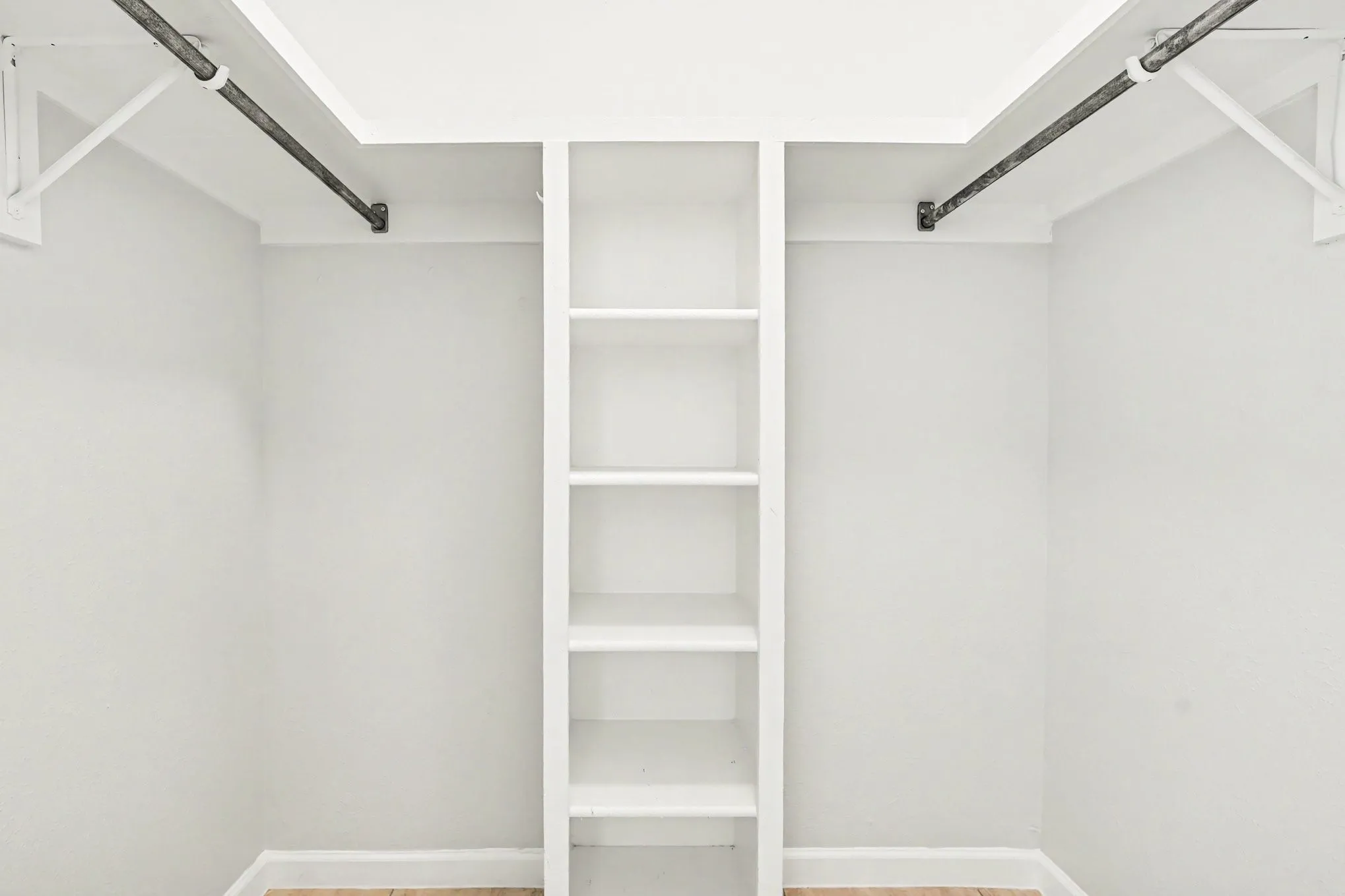 Both walk-in closets feature a central shelving unit, two hanging rods, light gray walls, white trim, and wood-finish flooring
