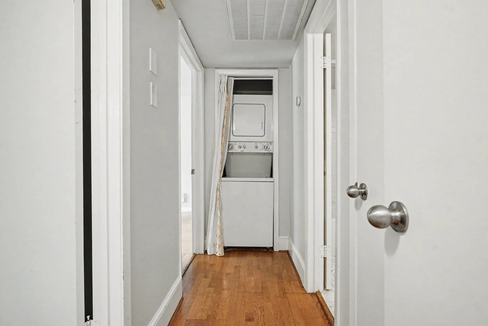 The hallway features wood-finish flooring, light grey wall paint, white trim, and a stackable washer and dryer at the end.  It also features a hall closet that would be ideal for linens and towels.