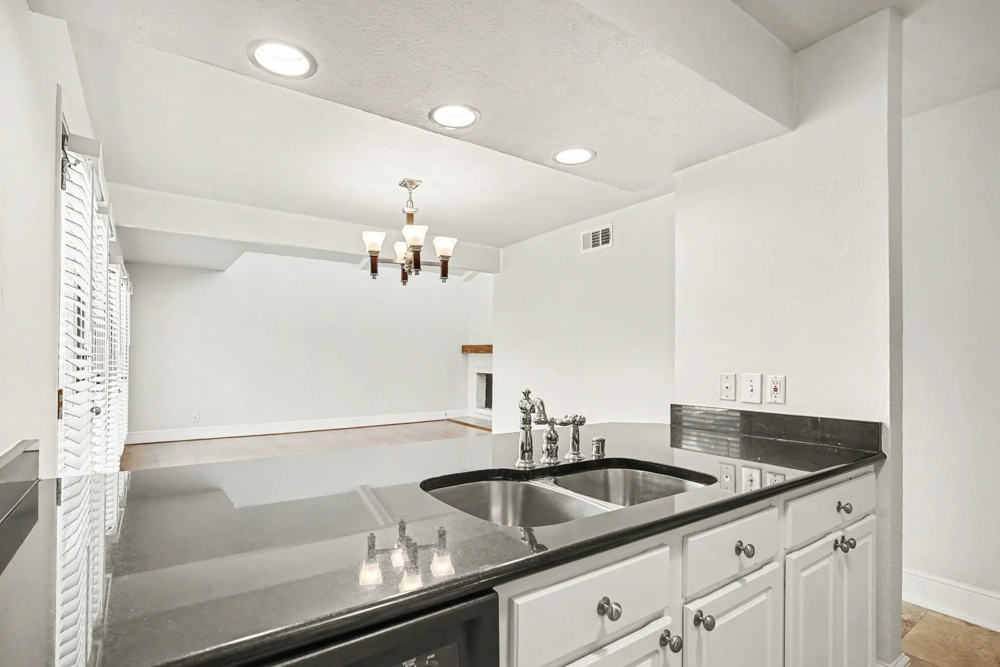 This kitchen view shows the double basin sink with goose neck chrome faucet, dark granite countertop, and white cabinetry.