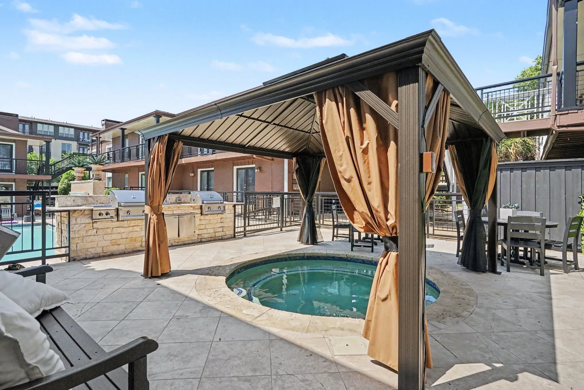 Separate covered spa, built-in BBQ station with multiple grills, tile flooring, and security fencing.