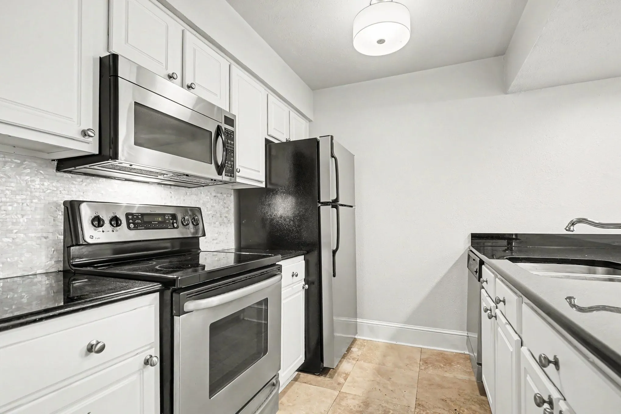 The kitchen features white cabinetry, dark granite countertops, stainless steel appliances, and an updated tiled backsplash.  The oven has a 5-burner cooktop with a convection feature.  The microwave has a vent feature, and the freezer has an ice maker.
