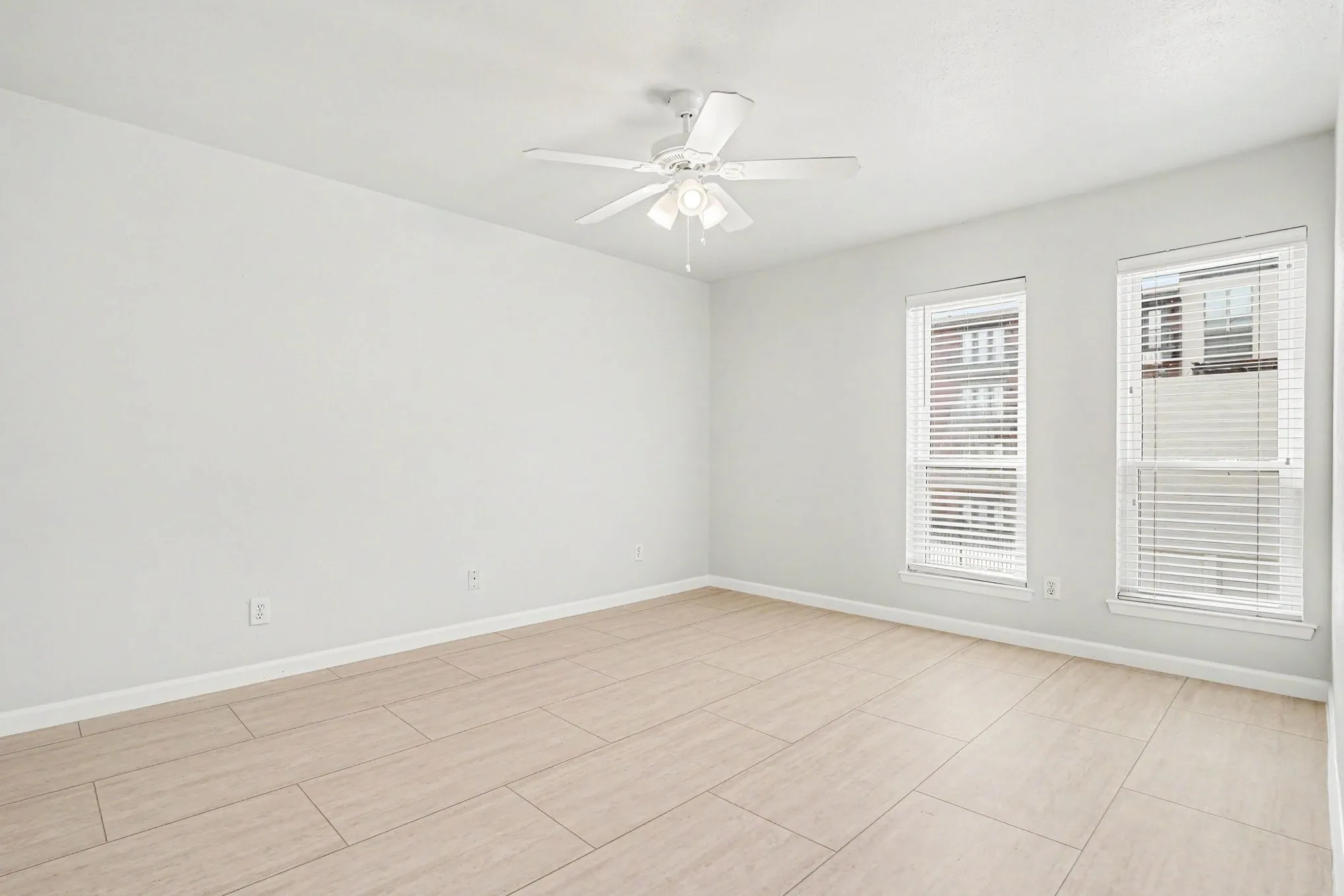 The second bedroom is also bright and features two windows with blinds, a ceiling fan, light-toned tile flooring, and a walk-in closet.