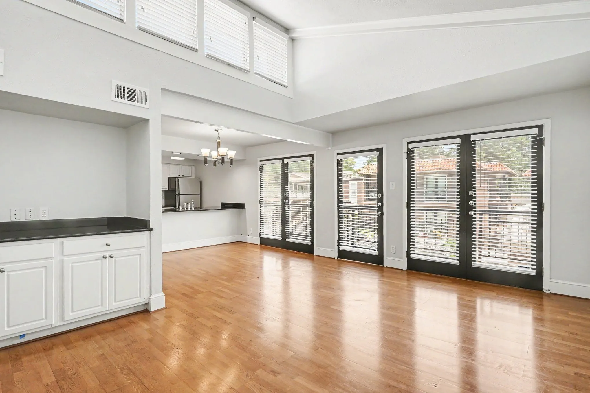 View from the fireplace toward kitchen showing front entry and two sets of adjacent French doors providing an abundance of natural light.  A built-in dry bar on the left provides extra storage and space for entertaining.