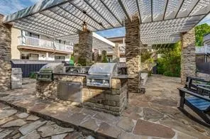 The second outdoor kitchen features dual built-in grills, a sink, and stone-clad cabinetry, all under a louvered pergola