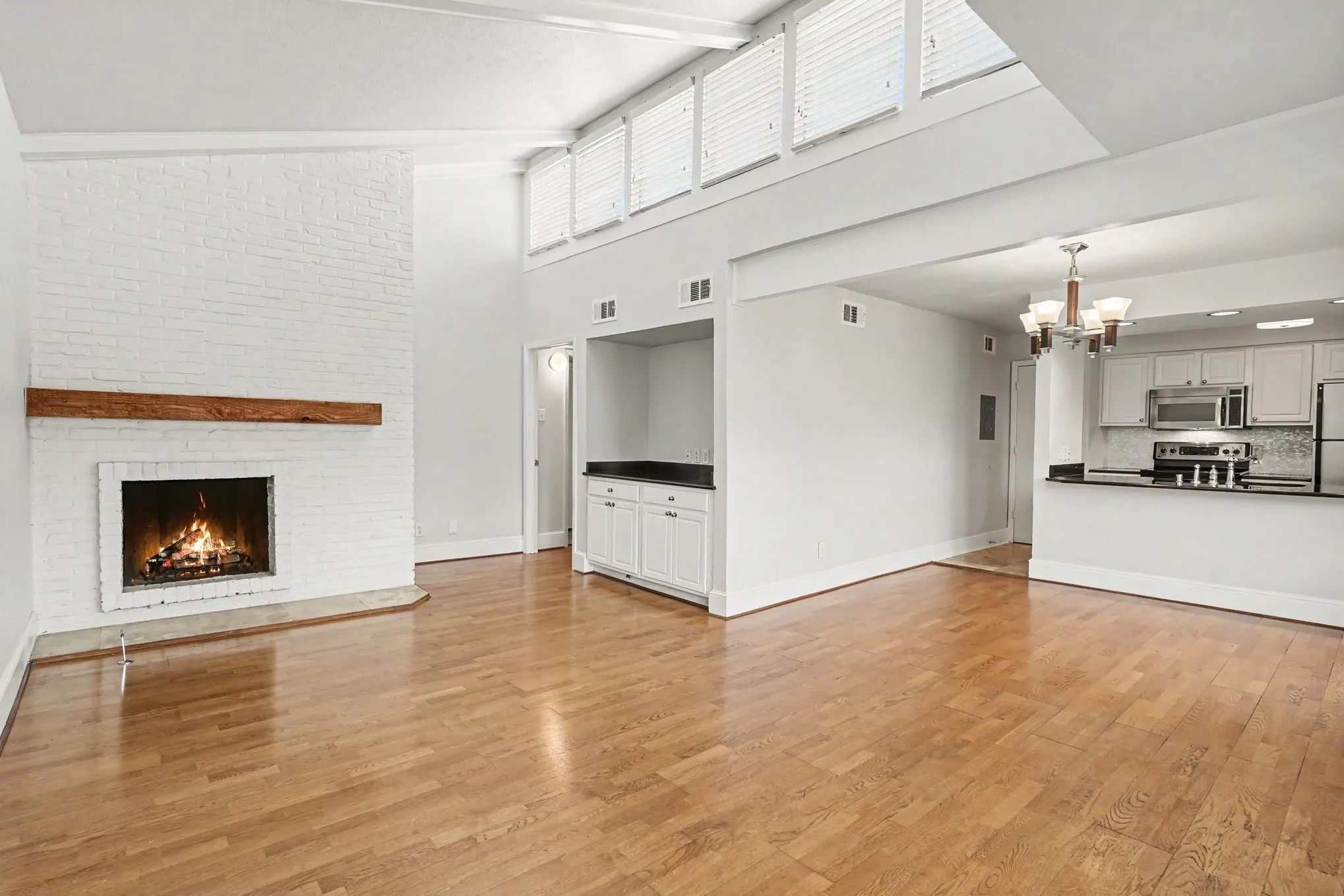 The living area features vaulted ceilings with clerestory windows, wood-finish flooring, a white brick gas log fireplace with a wood mantle, and an open concept kitchen with stainless steel appliances and a breakfast bar