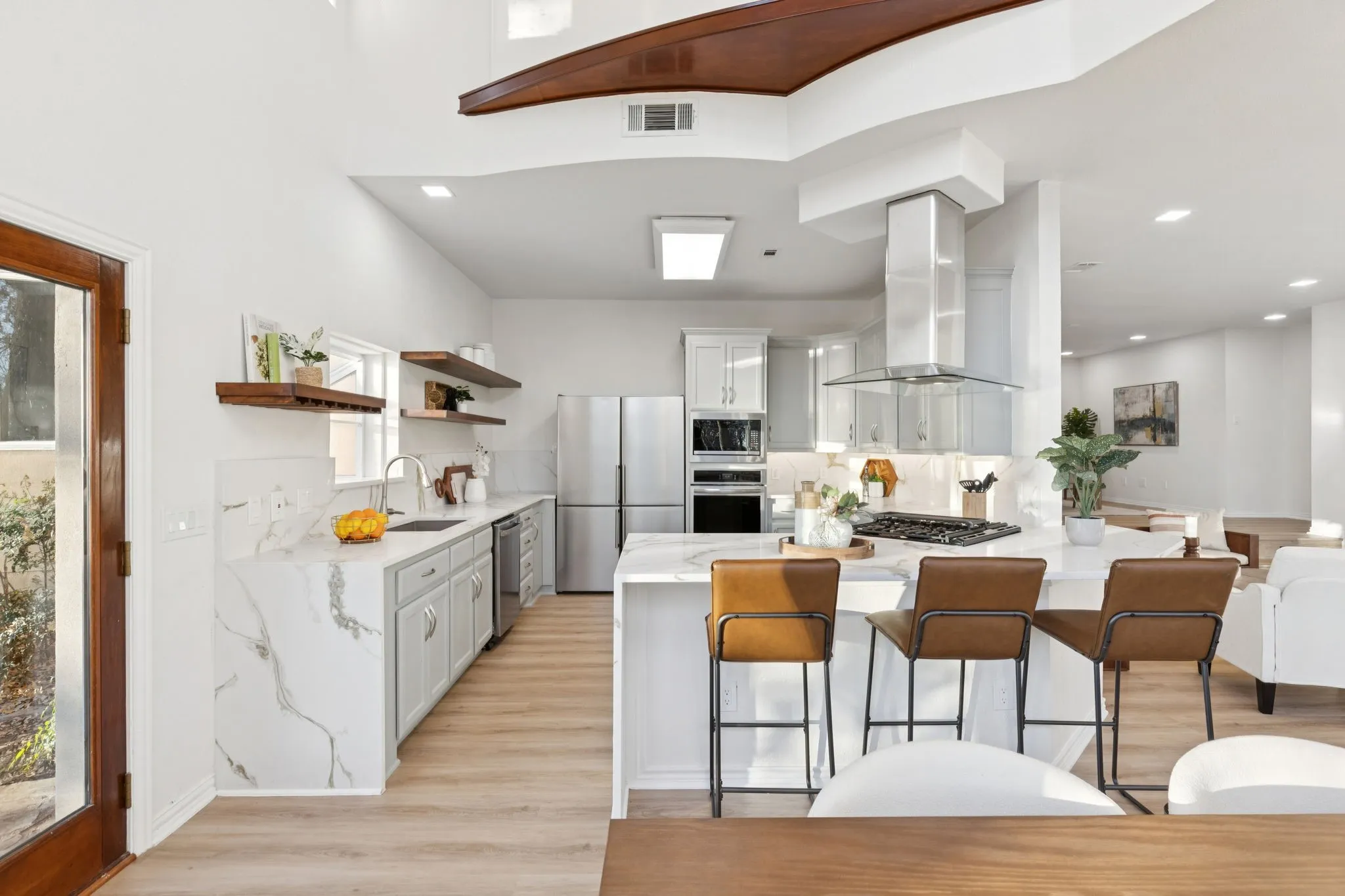 Kitchen with light stone countertops, a peninsula, appliances with stainless steel finishes, ventilation hood, and white cabinetry