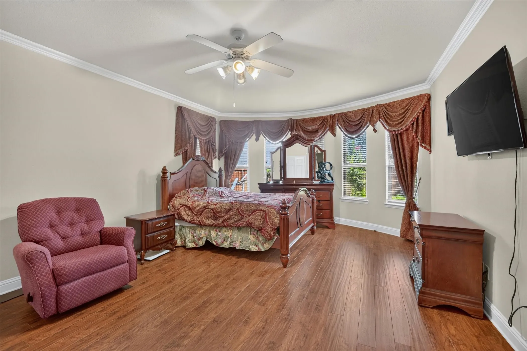 Spacious room featuring wood-finish flooring, a curved wall with multiple windows, crown molding, and a ceiling fan with integrated lighting