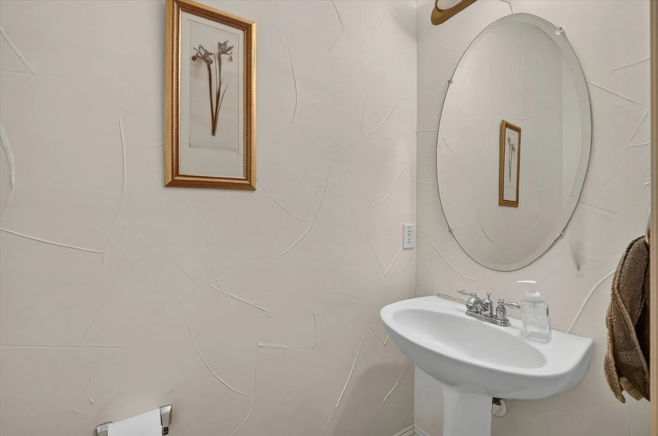 Pedestal sink with chrome faucet, complemented by an oval wall mirror