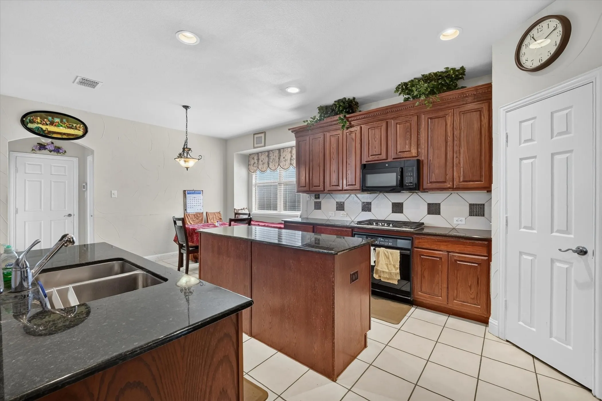 Kitchen featuring dark wood cabinetry, a central island with a granite-style countertop, a double basin sink, recessed lighting, and white tile flooring