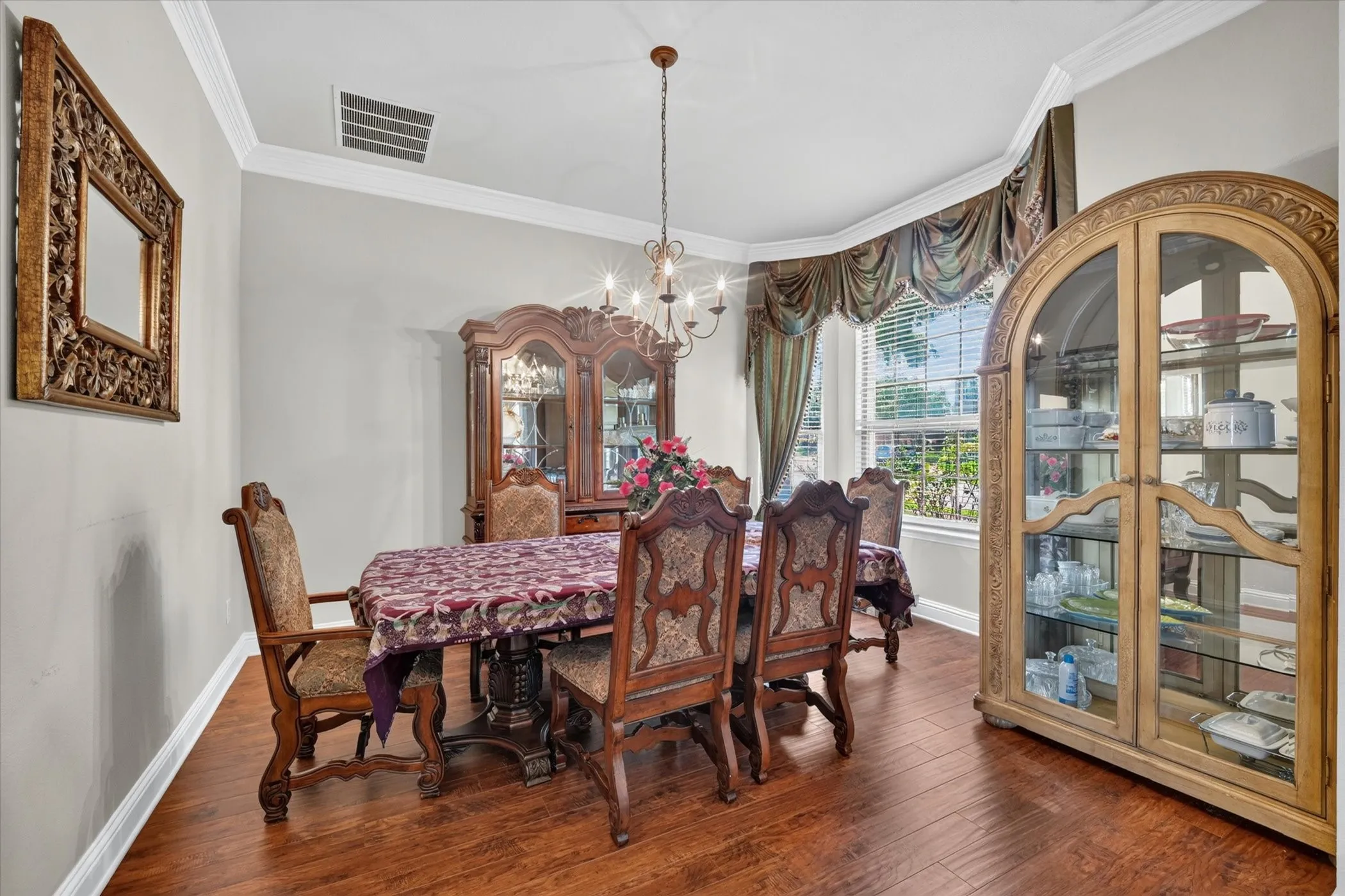 Spacious room featuring wood-finish flooring, a large bay window, crown molding, and a chandelier
