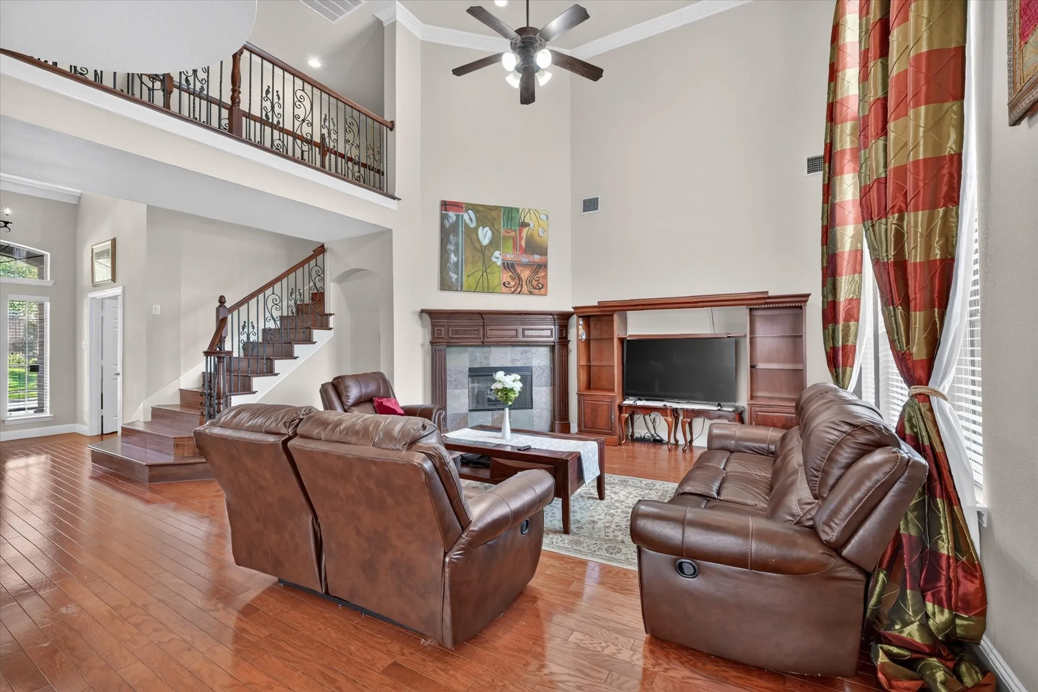 Two-story living area featuring wood-finish flooring, a contemporary ceiling fan, and a fireplace with a stone surround and wood mantel