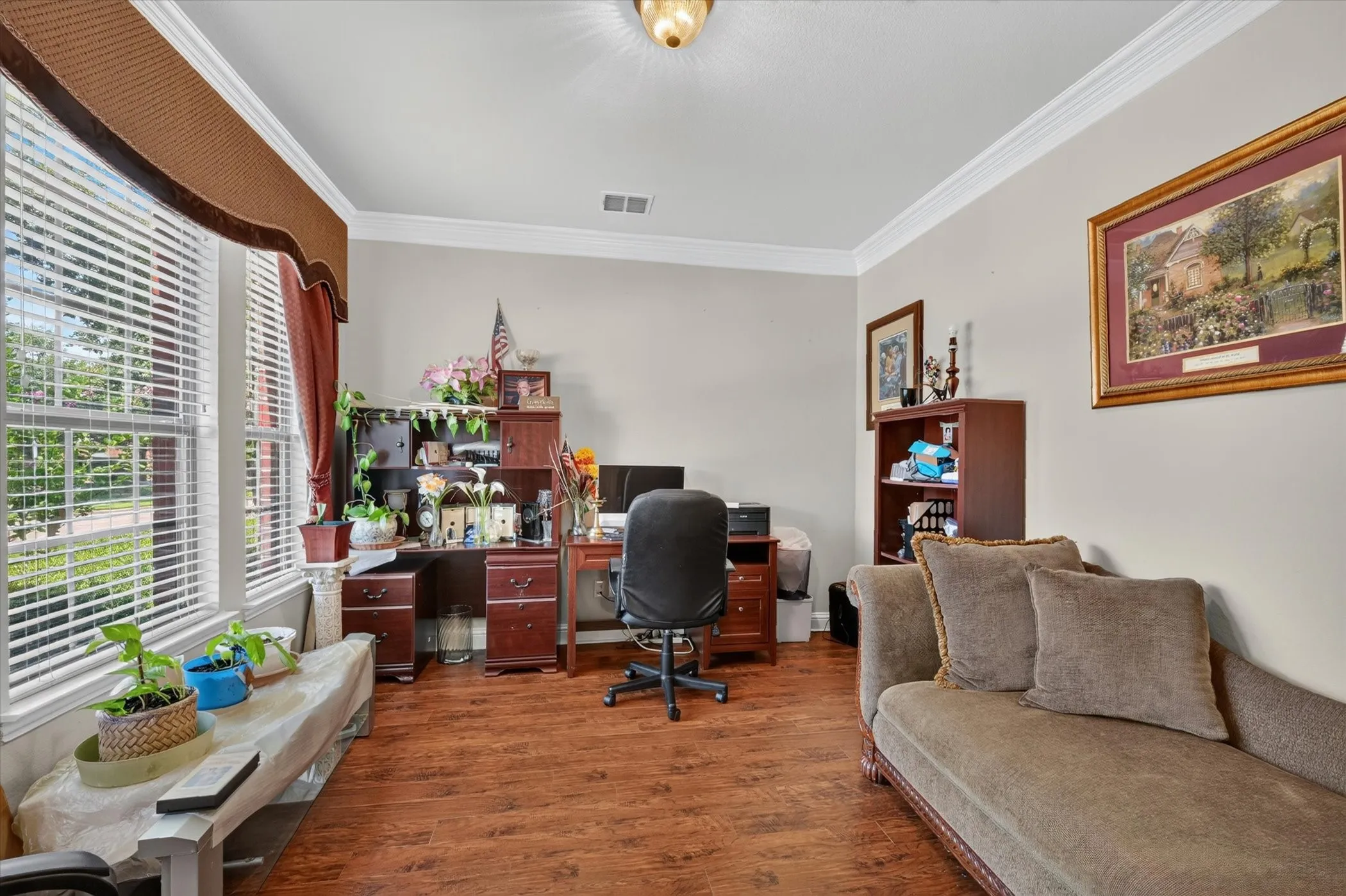 Spacious room featuring wood-finish flooring, crown molding, and large windows with blinds