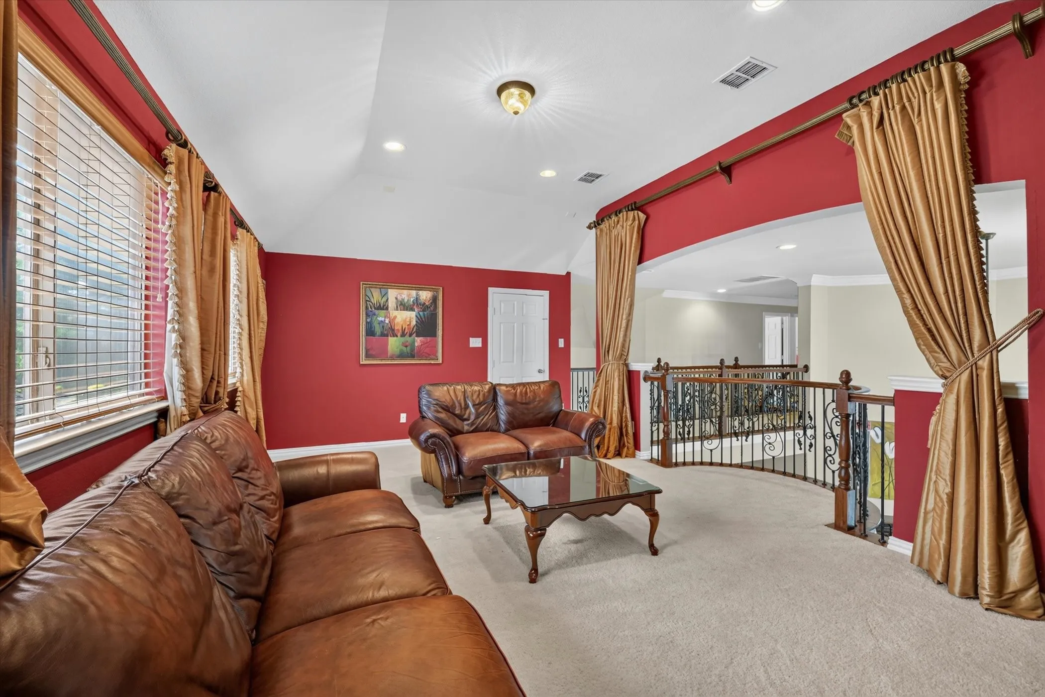 Carpeted lounge area featuring a curved wrought iron and wood railing, arched entryway, window with blinds, and recessed lighting