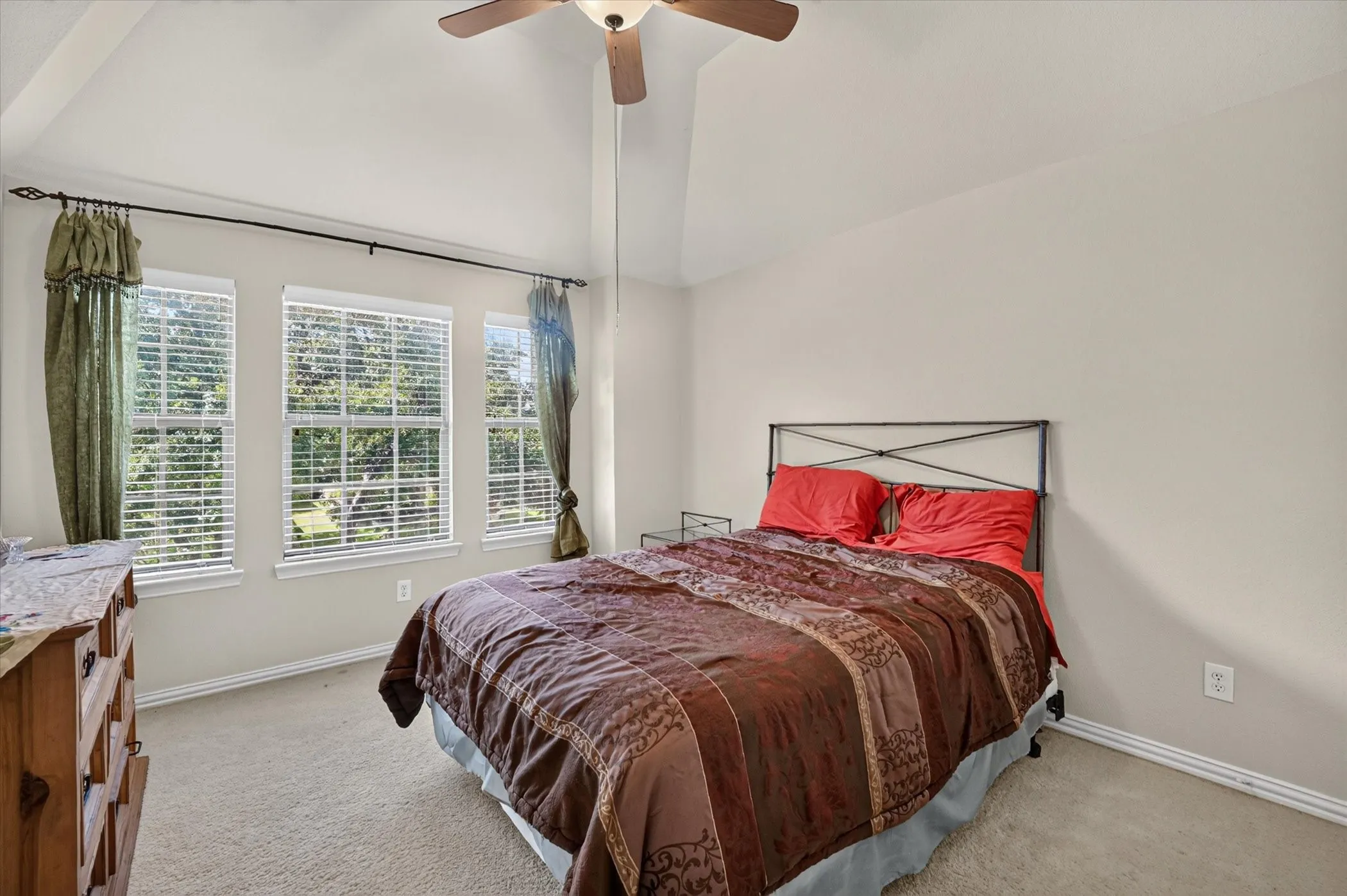Bedroom with vaulted ceiling, three windows with blinds, and a ceiling fan