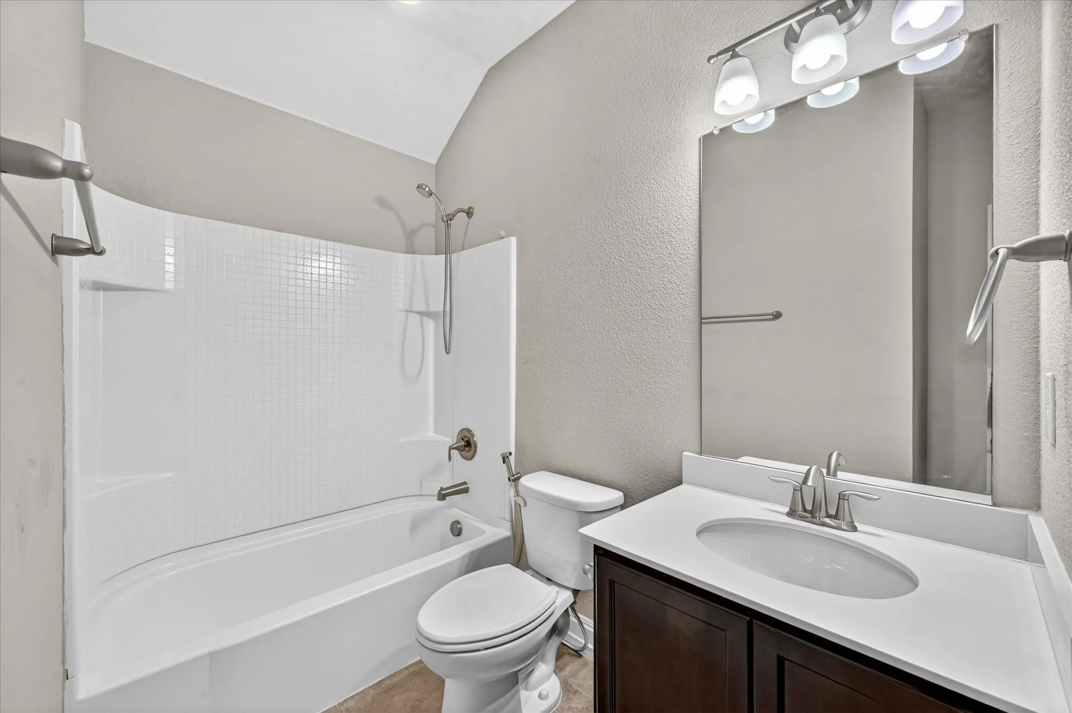 Bathroom featuring a white tub and shower combination with a textured surround, a dark wood-finish vanity with a white countertop and integrated sink, a large mirror, and brushed nickel fixtures