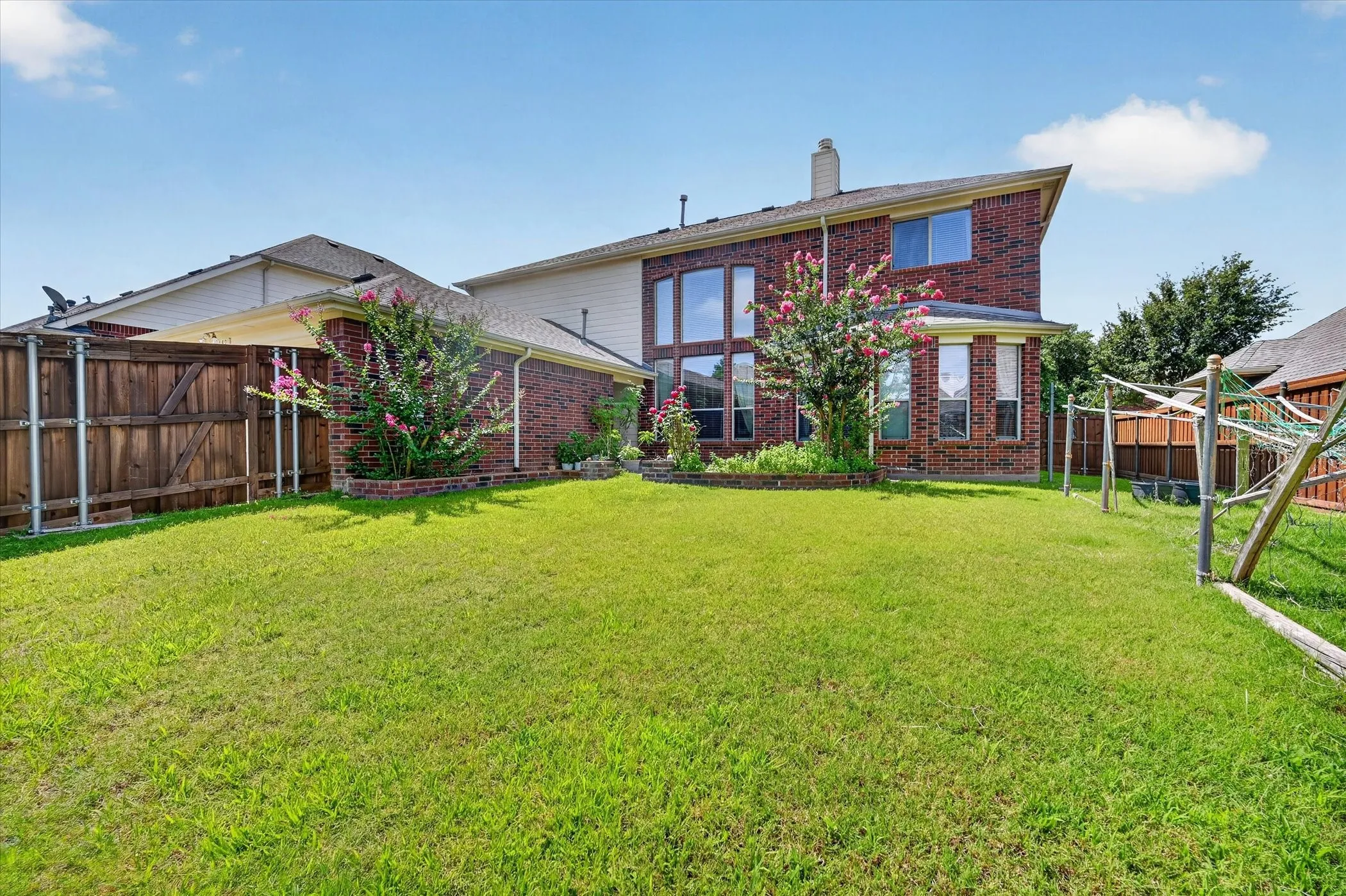 Expansive backyard featuring a manicured lawn, brick exterior, multiple large windows, and mature landscaping