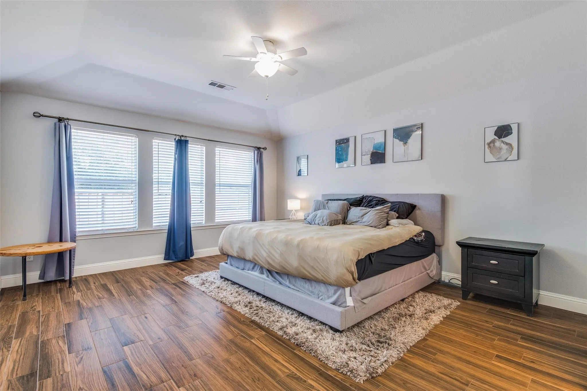 Spacious room featuring wood-finish flooring, a tray ceiling with a ceiling fan, and multiple windows with blinds