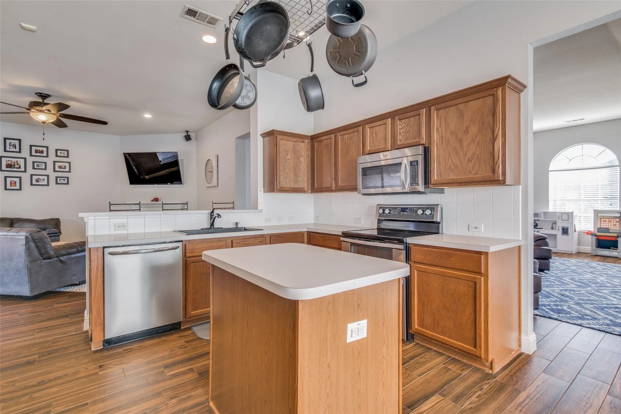 Kitchen featuring wood-finish flooring, a central island, light-toned countertops, wood cabinetry, and stainless steel appliances
