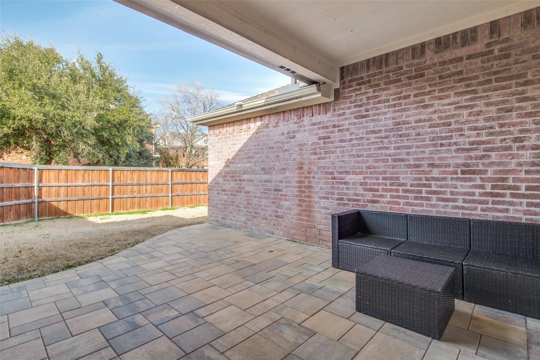 Covered outdoor patio featuring multi-toned paver flooring, brick exterior wall, and a wooden privacy fence