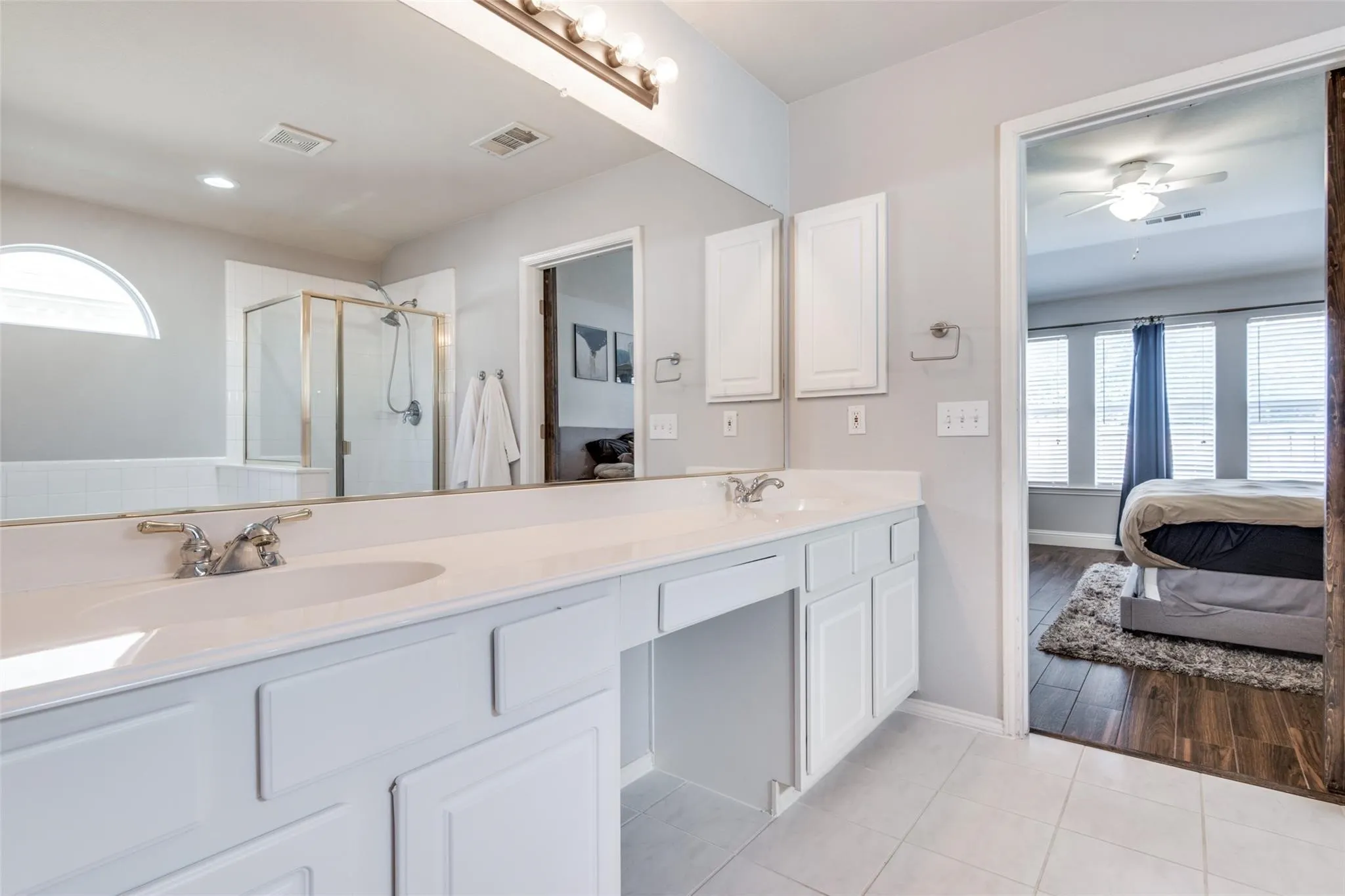 Bathroom vanity featuring dual undermount sinks with chrome fixtures, white cabinetry, and a light-colored countertop
