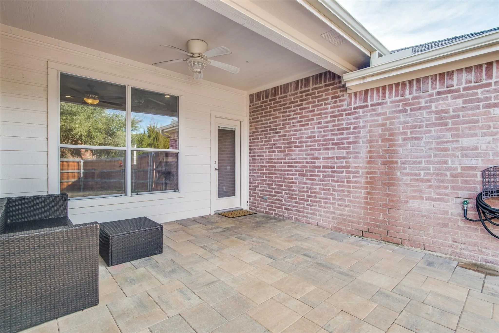 Covered patio featuring a ceiling fan, brick accent wall, white siding, and stone paver flooring
