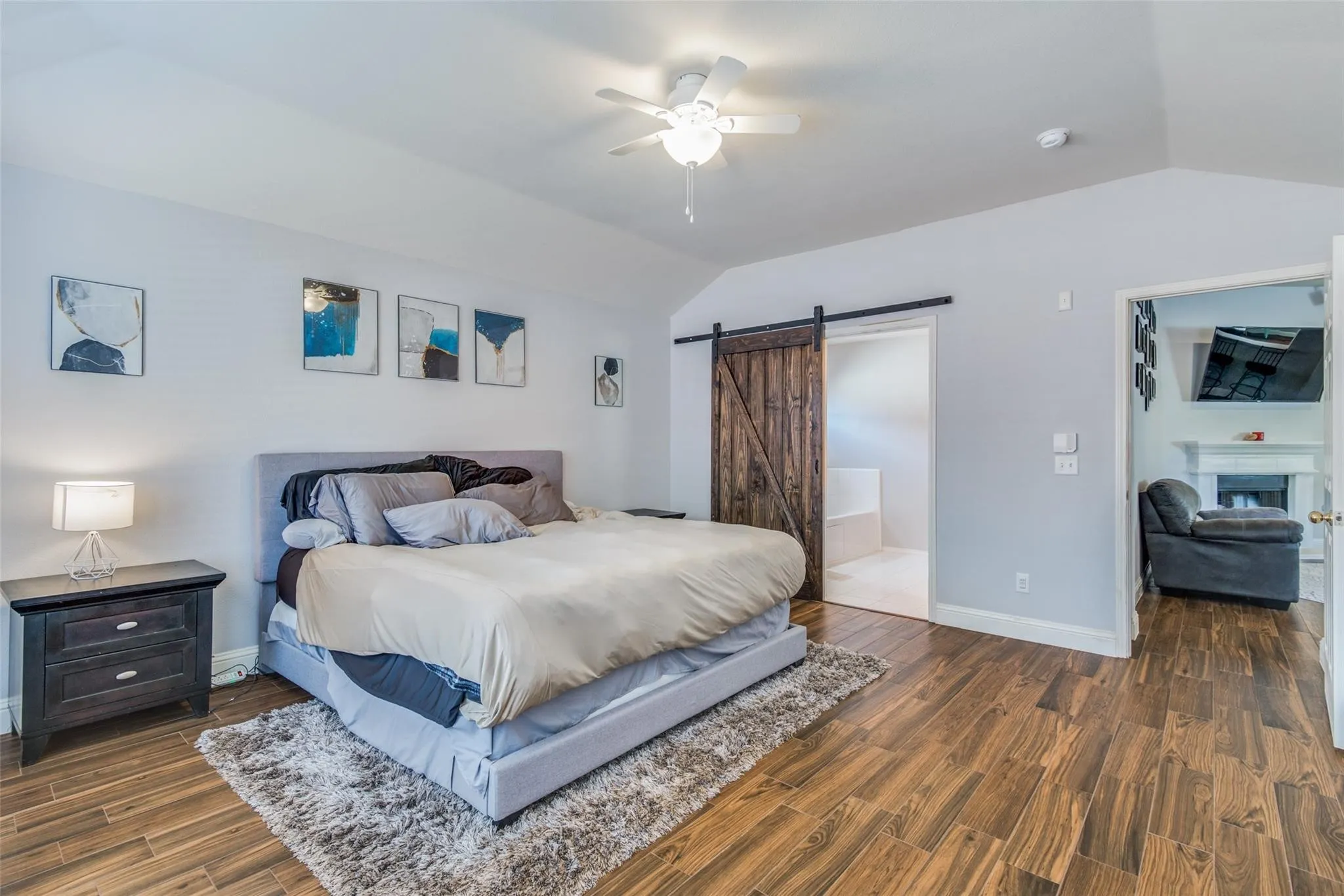 Vaulted ceiling featuring a ceiling fan, wood-finish flooring, a barn door, and a white baseboard trim