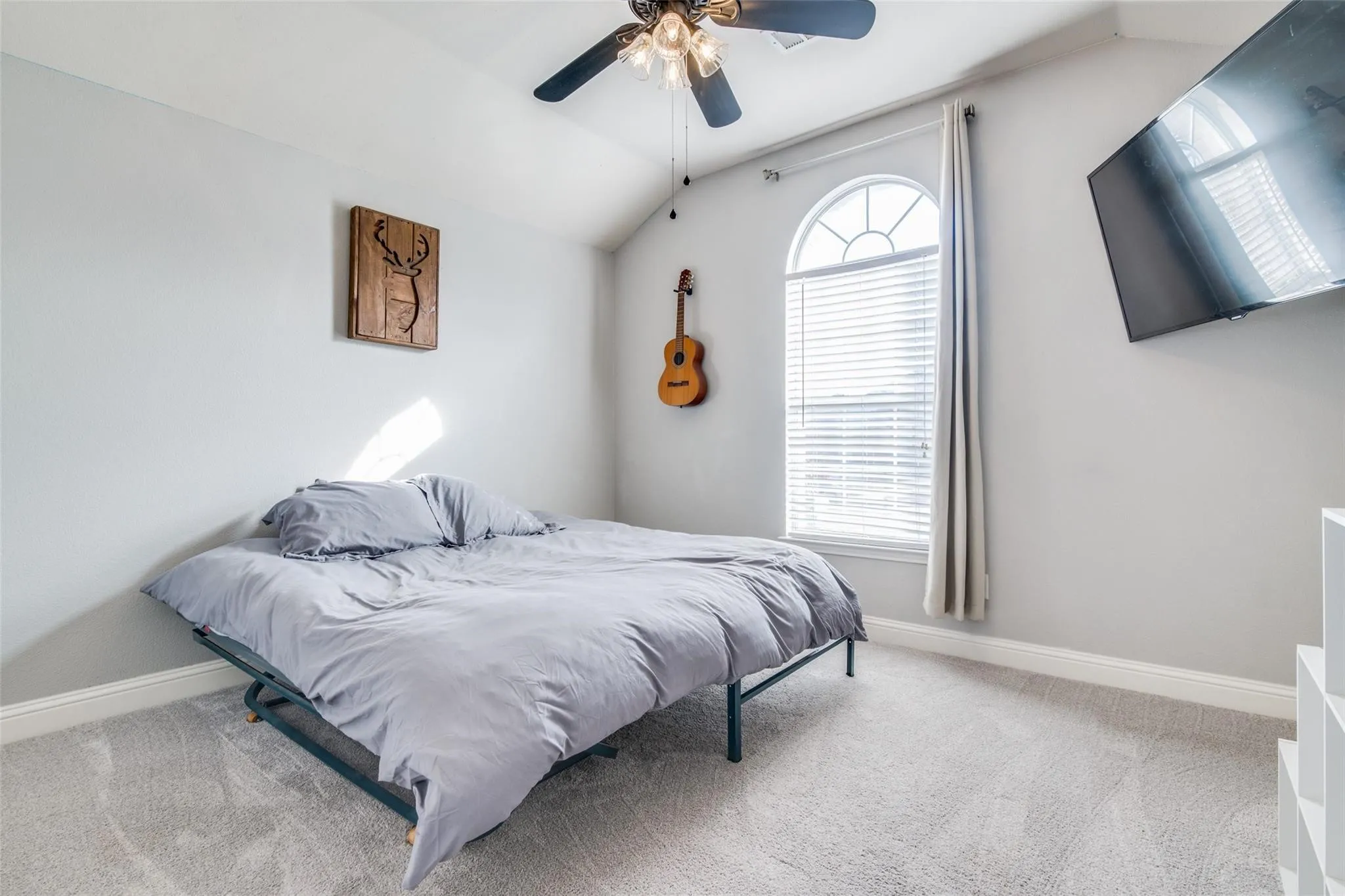 Carpeted room featuring a vaulted ceiling with a ceiling fan, an arched window with blinds and drapes, and white baseboards