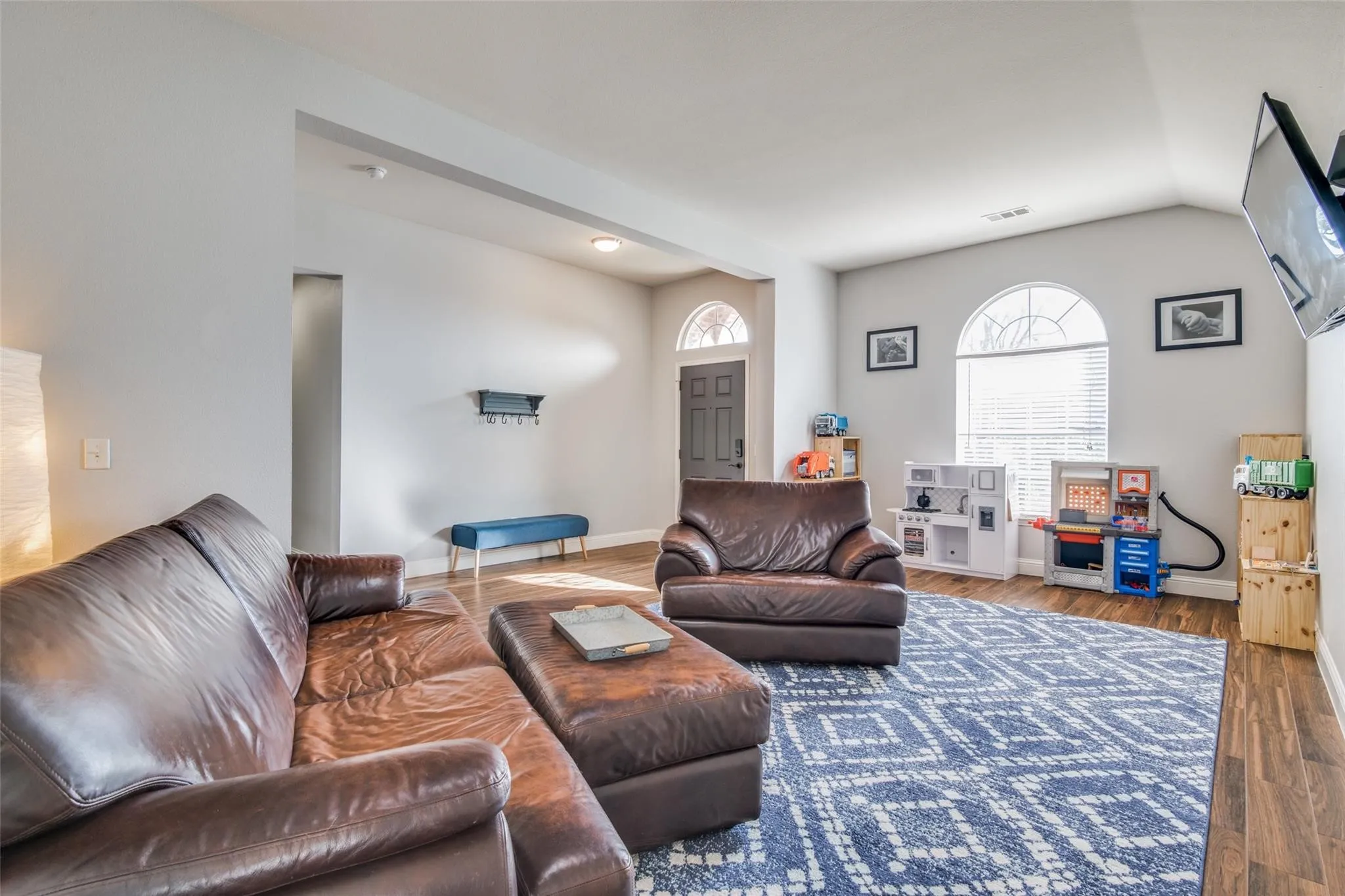 Spacious living area featuring wood-finish flooring, vaulted ceilings, and light gray wall tones