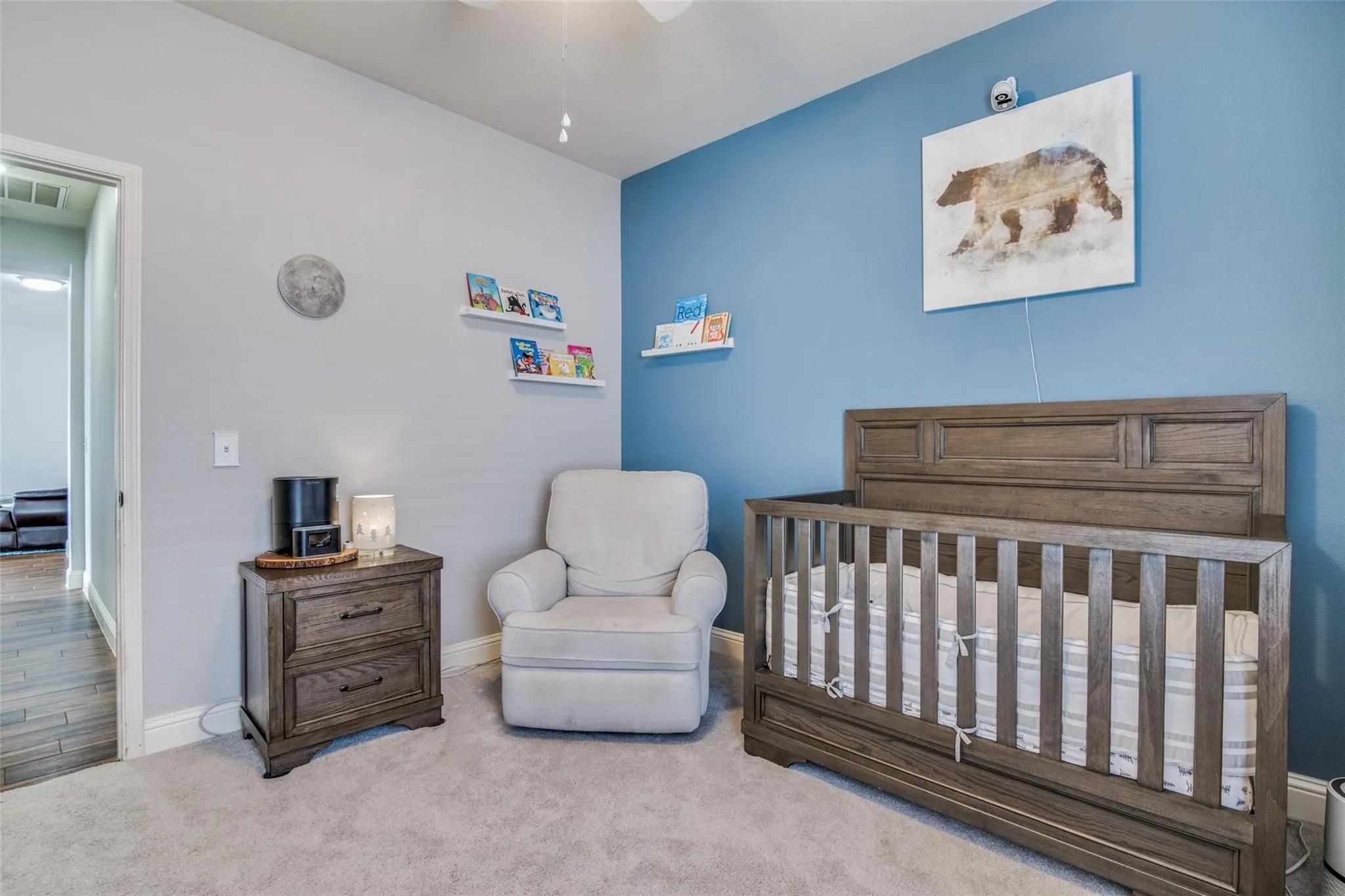 Carpeted room featuring a ceiling fan, light gray and blue accent walls, and a doorway opening to a hallway with wood-finish flooring