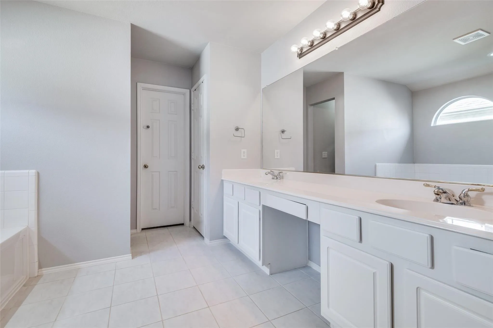 Bathroom featuring a double vanity with white cabinetry and integrated sinks, a large mirror, and tiled flooring